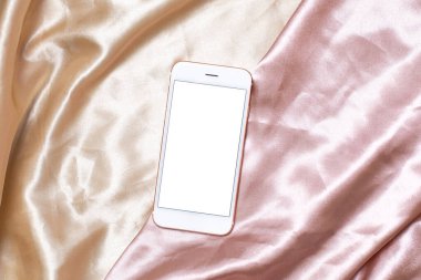 Bej ve pembe ipek üzerinde cep telefonu olan düz konsept kadınsı ışık arkaplanı. Üst görünümü olan beyaz ekran