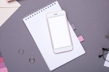 Gri arkaplan görünümlü beyaz not defteri ve nakışlı boş ekranlı cep telefonu