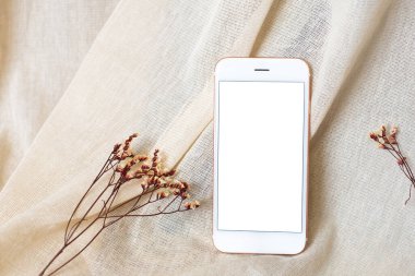 Bej doğal pamuk kumaş arka planında cep telefonu ve kuru çiçekler. Biçimli hisse senedi yan görünümü oluşturur