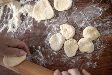 Son sınıf öğrencisi kadın, mutfak manzarasında hamuru un içinde yuvarlıyor.