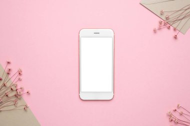 Beyaz ekranlı cep telefonu ve pembe arka planda kuru pembe çiçek dalı. Telif alanı üst görünümüne sahip en düşük konsept