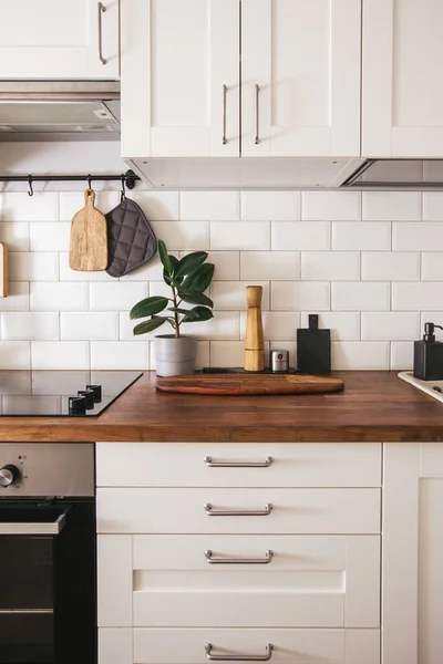 Mutfak aletleri, şef aksesuarları. Beyaz kiremitler duvar ve ahşap masa üstüyle asılı mutfak. Mutfak arka planında yeşil bitki dikey yan görünümü var.