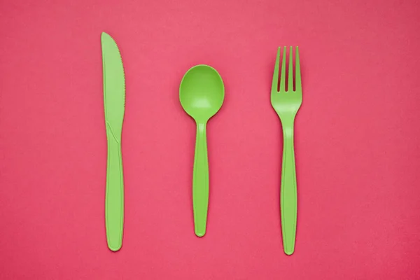 Green plastic forks, spoons, knifes on pink paper. Set of plastic cutlery in different spoons forks knives and eco-friendly plastic concept. Flat lay. Horizontal. Close-up top view