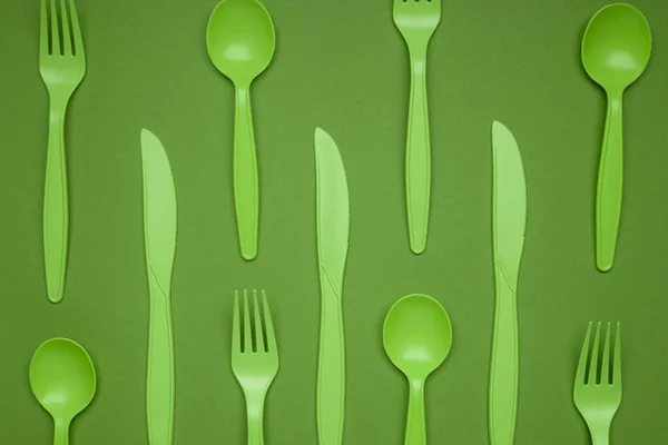 Green plastic forks, spoons, knifes on green paper. Set of plastic cutlery in different spoons forks knives and eco-friendly plastic concept. Flat lay. Horizontal. Close-up top view