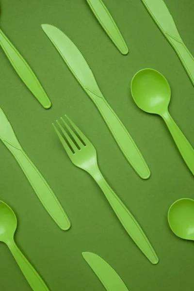Green plastic forks, spoons, knifes on green paper. Set of plastic cutlery in different spoons forks knives and eco-friendly plastic concept. Flat lay. Close-up top vertical view