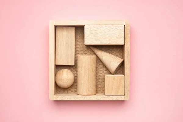 Wooden figures in box on pink background. Abstract background of wooden objects. Geometric composition. Scene with geometrical forms top view