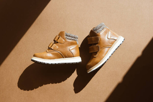 Пара маленьких кожаных туфель на светлом коричневом фоне с солнечной тенью. Теплая, меховая детская обувь со шнурками. Концепция предстоящего осенне-зимнего вида сверху