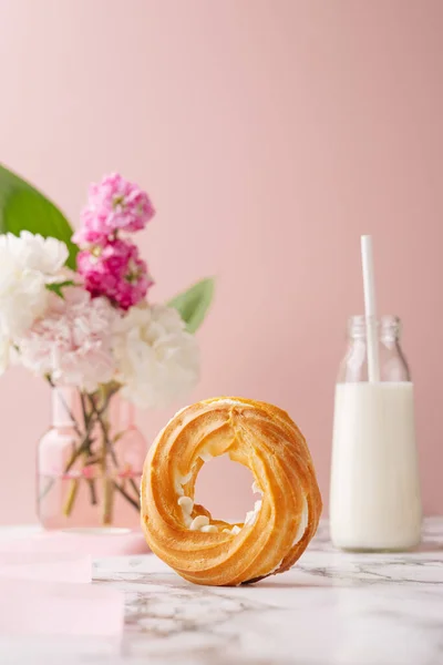 Círculo caseiro profiterole com creme de açúcar em pó coberto sobre mesa de mármore sobre fundo rosa com flores e leite — Fotografia de Stock
