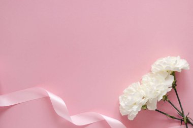 Anneler Günün kutlu olsun. Kurdeleli beyaz çiçek, pembe pastel arka planda, telif alanı üst görüşlü.