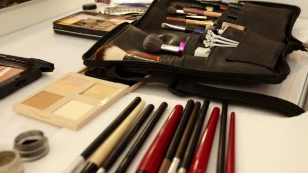 Materiały do makijażu kobiety przygotowującej się do ważnego wydarzenia, paleta kosmetyków, szminka, pędzle na białym stole — Wideo stockowe