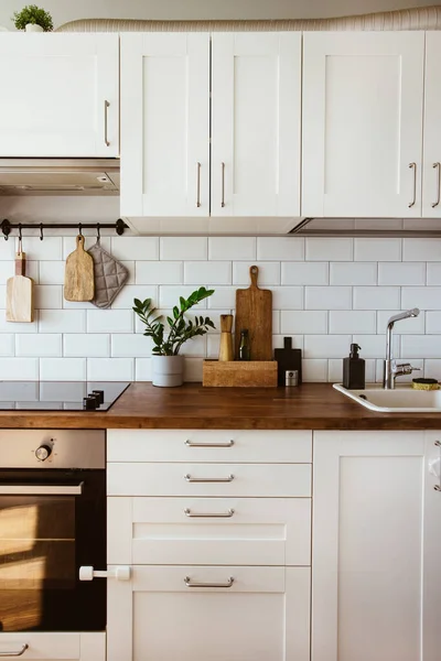 Kitchen brass utensils, chef accessories. Hanging kitchen with white tiles wall and wood tabletop.Green plant on kitchen background