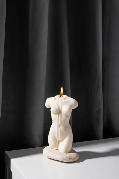 Candle in woman torso shape burning in grey interior in slow motion, atmosphere and smoke after candle