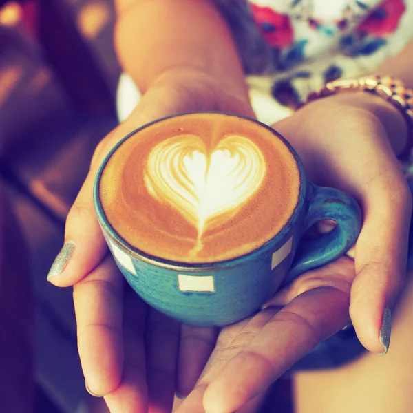 Mano y taza de café latte arte en el fondo de madera vintage — Foto de Stock