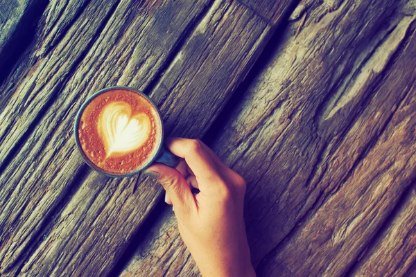 Hand en kopje koffie latte kunst op de houten achtergrond vintage — Stockfoto