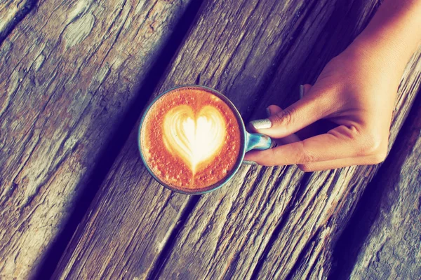 Main et tasse de café latte art sur le fond bois vintage — Photo