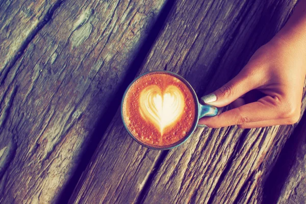 Mano y taza de café latte arte en el fondo de madera vintage — Foto de Stock