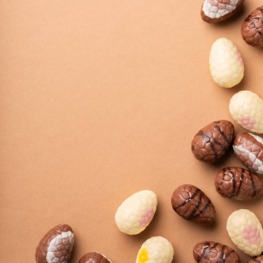 Renkli çikolatalı Paskalya yumurtaları, farklı tasarım ve dokulara sahip kahverengi bir yüzeye saçılmış olup, şenlikli kutlamalar ve fotokopi alanı ile dekorasyonlar için idealdir.