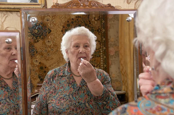 Senior woman puts on lipstick — Stock Photo, Image