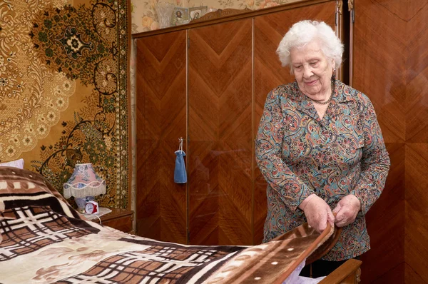 Старшая женщина застилает постель — стоковое фото