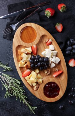 Atıştırmalık ve aperatifler. Bal, üzüm, çilek, biberiye ve fındıklı peynir tabağı siyah bir masanın üzerinde. Restoran menüsü. Arkaplan resmi, kopyalama alanı. Flatlay, üst görünüm
