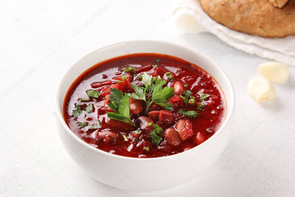 Russian and Ukrainian cuisine. Borscht with beans in a white bowl. Garlic and tortillas on a white table. Beetroot, bean, potato soup with parsley. Background image, copy space