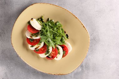 İtalyan mutfağı. Caprese. Mozzarella, domates, pesto soslu roka ve gri arka planda bej bir tabakta zeytinyağı. Restoran menüsü. Arkaplan resmi, kopyalama alanı. Flatlay, üst görünüm