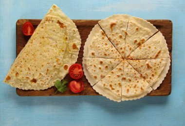 Doğu Özbek mutfağı. Peynirli ve domatesli ince hamurdan yapılmış yassı ekmek. Pitcha non. Sülüguni ve ahşap bir tahtanın üzerinde bitkiler olan kutbiler. Arkaplan resmi, kopyalama alanı. Flatlay, üst görünüm