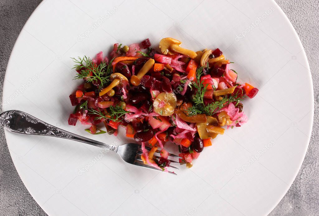 Russian cuisine. Snacks. Beetroot salad with mushrooms. Salad with beets, mushrooms, cabbage, carrots and potatoes on a white plate. Restaurant menu. Background image, copy space. Top view, flatlay