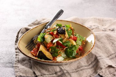 Doğu mutfağı. Bay Chaw 'ın salatası. Kızarmış patlıcan, domates, salatalık, kırmızı biber, soğan ve gri bir masada bej bir tabakta soslu taze otlardan salata. Arkaplan resmi, alanı kopyala