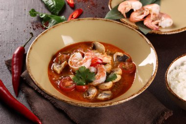 Tayland mutfağı. Tom lezzetli. Karidesli hindistan cevizi sütü çorbası, mantar, domates, galangal kökü, limon otu, kahverengi bir masada bej bir kasede kırmızı biber. Pirinç. Arkaplan resmi, alanı kopyala