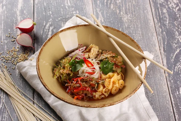 Korean cuisine. Kuksi. Korean soup with veal, wheat noodles, pickled cabbage, cucumbers, radish, omelette, asparagus and chili pepper in a bowl with chopsticks on wooden table. Background image — Stock Image Korean Cuisine Kuksi Korean Soup Veal Wheat Noodles Pickled Cabbage Stock Photo