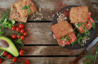 Sağlıklı yiyecekler. - Öğle yemeği. Kırmızı balıklı sandviç, krem peynir, avokado, roka ve tohum eski ahşap bir masada kahverengi bir tahta üzerinde. Rustik. Üst Manzara, düz çizgi. Arkaplan resmi, alanı kopyala
