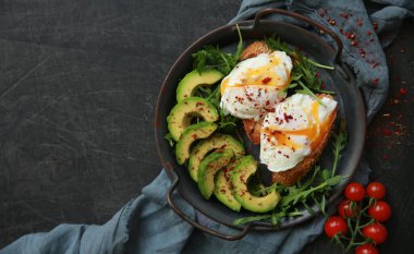 Sağlıklı kahvaltı. Kavrulmuş yumurta, roka, avokado, baharat ve kiraz domatesleri siyah bir masada gri bir tabakta. Arkaplan resmi, kopyalama alanı, yatay. Üst görünüm, düz görünüm