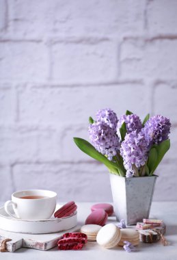 Bahar atmosferi. Vazodaki çiçekler, makarna, çikolata ve masa üzerindeki ahşap beyaz tahtalar üzerinde bir fincan çay. Leylak sümbülleri. Arkaplan resmi, kopyalama alanı, dikey, kırsal