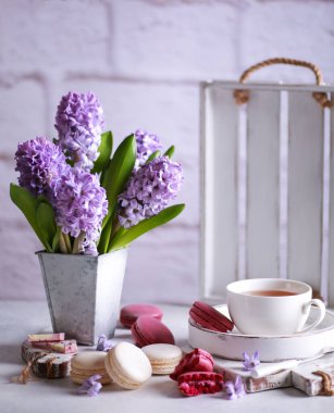Bahar atmosferi. Vazodaki çiçekler, makarna, çikolata ve masa üzerindeki ahşap beyaz tahtalar üzerinde bir fincan çay. Leylak sümbülleri. Arkaplan resmi, kopyalama alanı, dikey, kırsal
