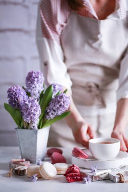 Bahar atmosferi. Vazoda çiçekler, makarna, çikolata ve bir bardak çay. Elleri olan bir lamba masasında tahta beyaz tahtalar üzerinde. Leylak sümbülleri. Arkaplan resmi, kopyalama alanı, dikey, kırsal