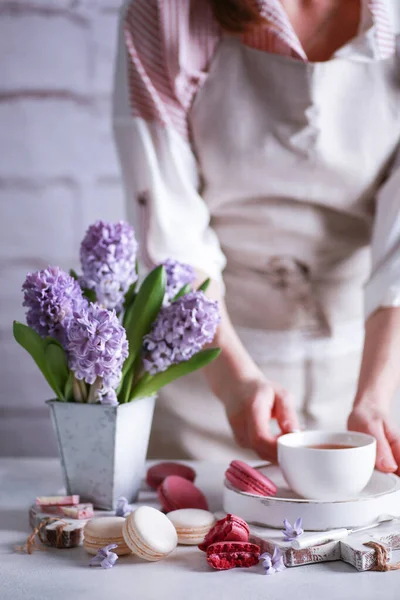Bahar atmosferi. Vazoda çiçekler, makarna, çikolata ve bir bardak çay. Elleri olan bir lamba masasında tahta beyaz tahtalar üzerinde. Leylak sümbülleri. Arkaplan resmi, kopyalama alanı, dikey, kırsal