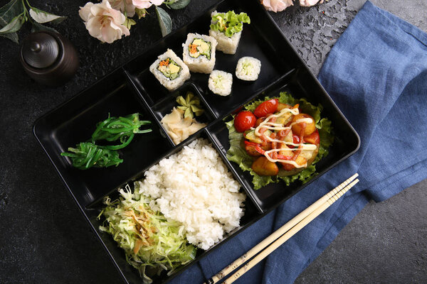 Japanese cuisine. Business lunch in a black box: rice, rolls, salad, sushi on a black table. Background image, copy space