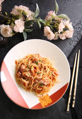 Siyah bir masada kırmızı ve beyaz tabakta sebzeli, peynirli ve otlu makarna. Sakura, yemek çubukları. Sebzeli erişte. Restoran menüsü. Arkaplan resmi, alanı kopyala