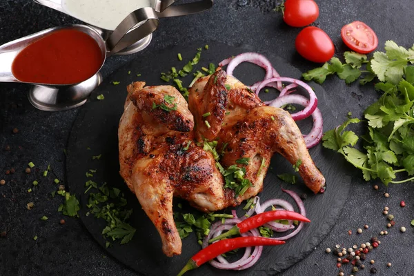 Fried chicken with fresh herbs, coriander, vegetables, onions, spices and sauces on a black table. Tobacco chicken. Background image, copy space