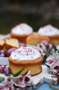 Paskalya. Bahar. Renkli yumurtalı Paskalya pastası, mavi bir masada beyaz tahta üzerinde çiçekler. Arkaplan resmi, kopyalama alanı, dikey