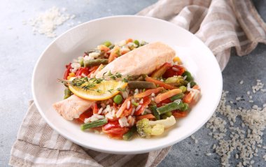 Deniz ürünleri tabağı. Pirinç ve sebzeli kırmızı balık. Limonlu somon, fasulye, havuç, bezelye ve gri bir masada beyaz bir tabakta karnabahar. Arkaplan resmi, alanı kopyala