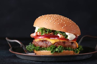 Fast food. Sığır etli, peynirli, pastırmalı ve sebzeli burger: siyah bir masada domates, soğan, lahana ve sos. Arkaplan resmi, alanı kopyala