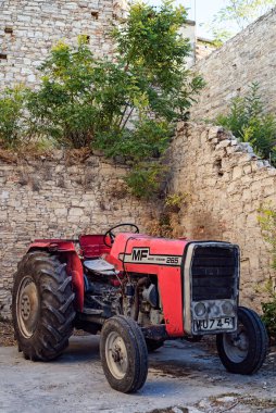 Eski kırmızı traktör, Kıbrıs Rum Kesimi 'nin duvarında yetişen eski taş duvarın arkasında duruyor.