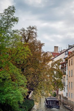 Prag, Çek Cumhuriyeti ve Avrupa 'daki eski şehrin mimarisi arasındaki dar kanal. Bir turist teknesi nehir boyunca yol alır, kıyıda bir park vardır, büyük yeşil ağaçlar büyür ve ördekler oturur.