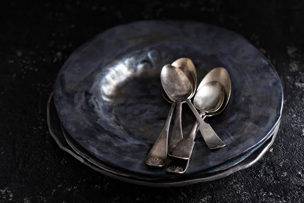 Black handmade ceramic plates with vintage spoons — Stock Photo, Image