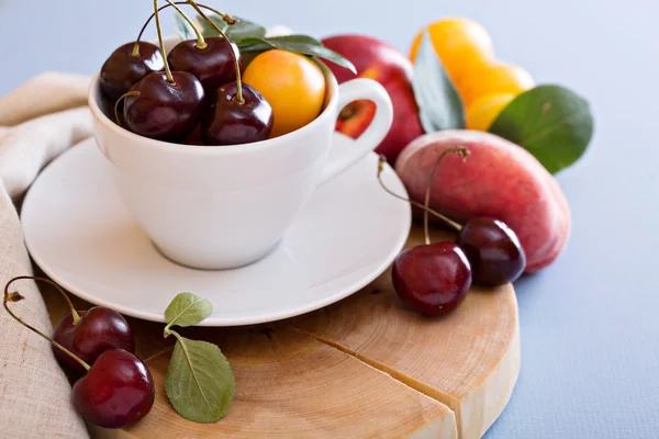 Frutas de hueso fresco y cerezas en taza blanca —  Fotos de Stock