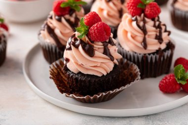 Sevgililer Günü 'nde üzerinde ahududu ve çikolata sosu olan pembe kremalı ahudududulu kekler.