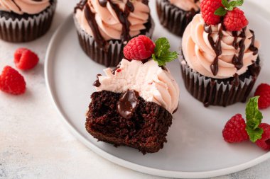 Sevgililer Günü 'nde üzerinde ahududu ve çikolata sosu olan pembe kremalı ahudududulu kekler.