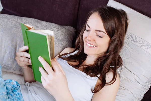 Kvinna ligger i sängen medan du läser en bok — Stockfoto